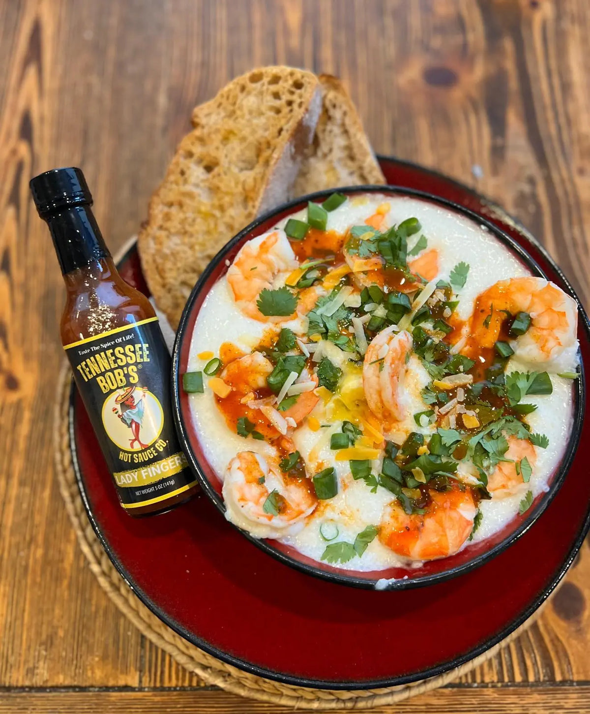 Bowl of cheesy shrimp and grits topped with green onions, cilantro, and Lady Fingers Hot Sauce