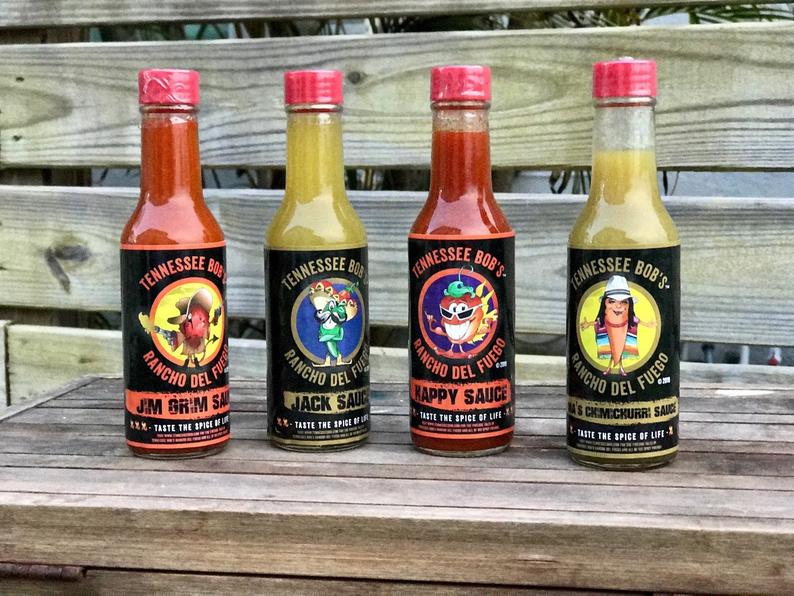 Four bottles of Tennessee Bob's hot sauce on a wooden surface with a blurred background.