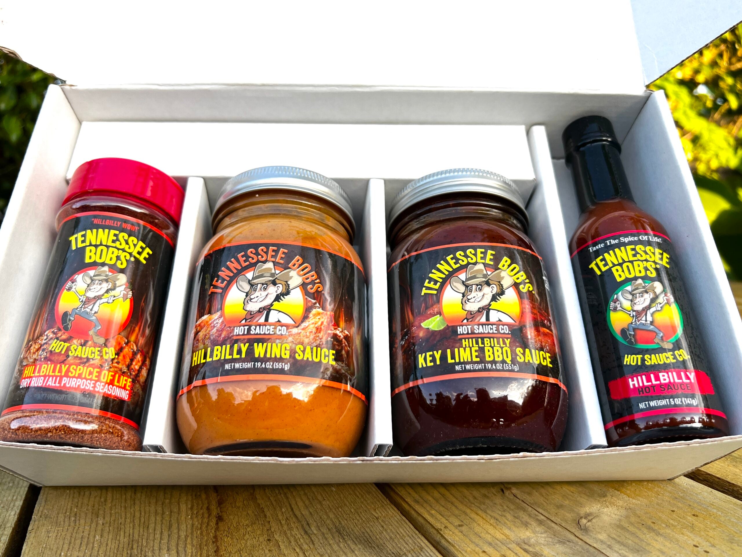 Four bottles of Tennessee Bob's hot sauces in a box on a wooden surface.