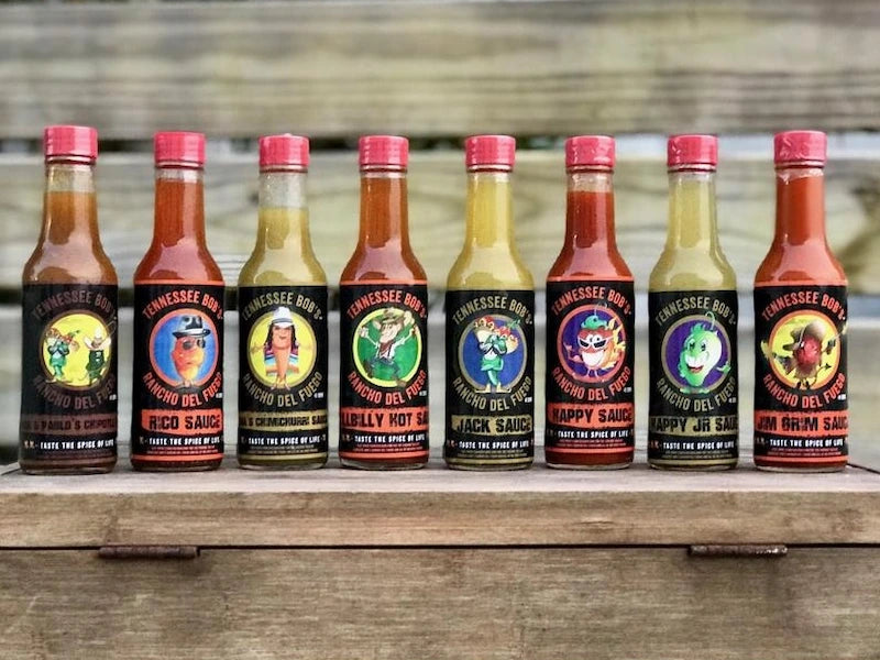 Row of Tennessee Bob hot sauce bottles with colorful labels on a wooden surface.