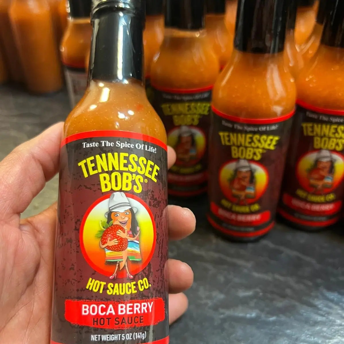 Hand holding a bottle of Tennessee Bob's hot sauce Boca Berry with more bottles in the background.