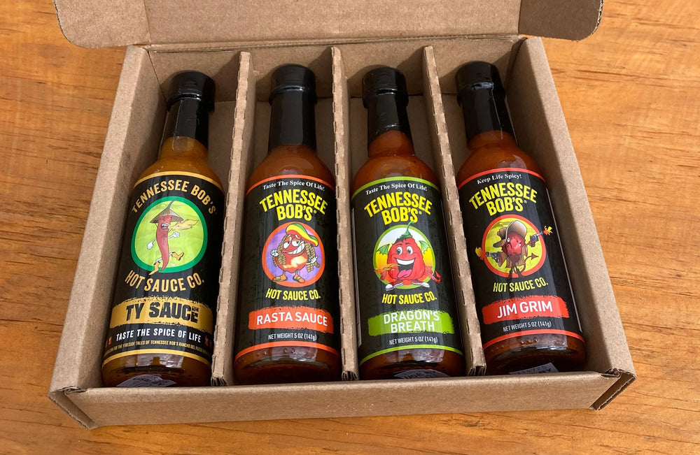 Four Tennessee Bob's hot sauce bottles in a cardboard box, featuring Ty Sauce, Rasta Sauce, Dragon's Breath, and Jim Grim flavors.