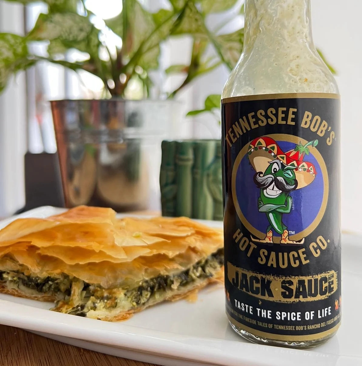 Bottle of Tennessee Bob's Hot Sauce Co. Jack Sauce with a dish of food in the background