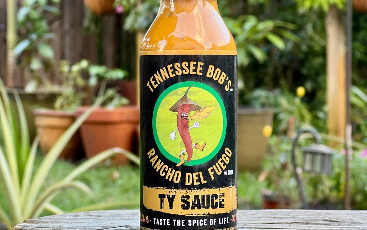 Bottle of Tennessee Bob's Rancho Del Fuego Ty Sauce on a wooden surface with a garden background