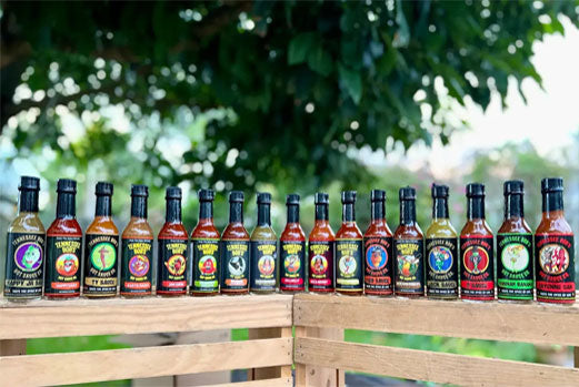 Assorted hot sauce bottles arranged on a wooden crate with a leafy background.