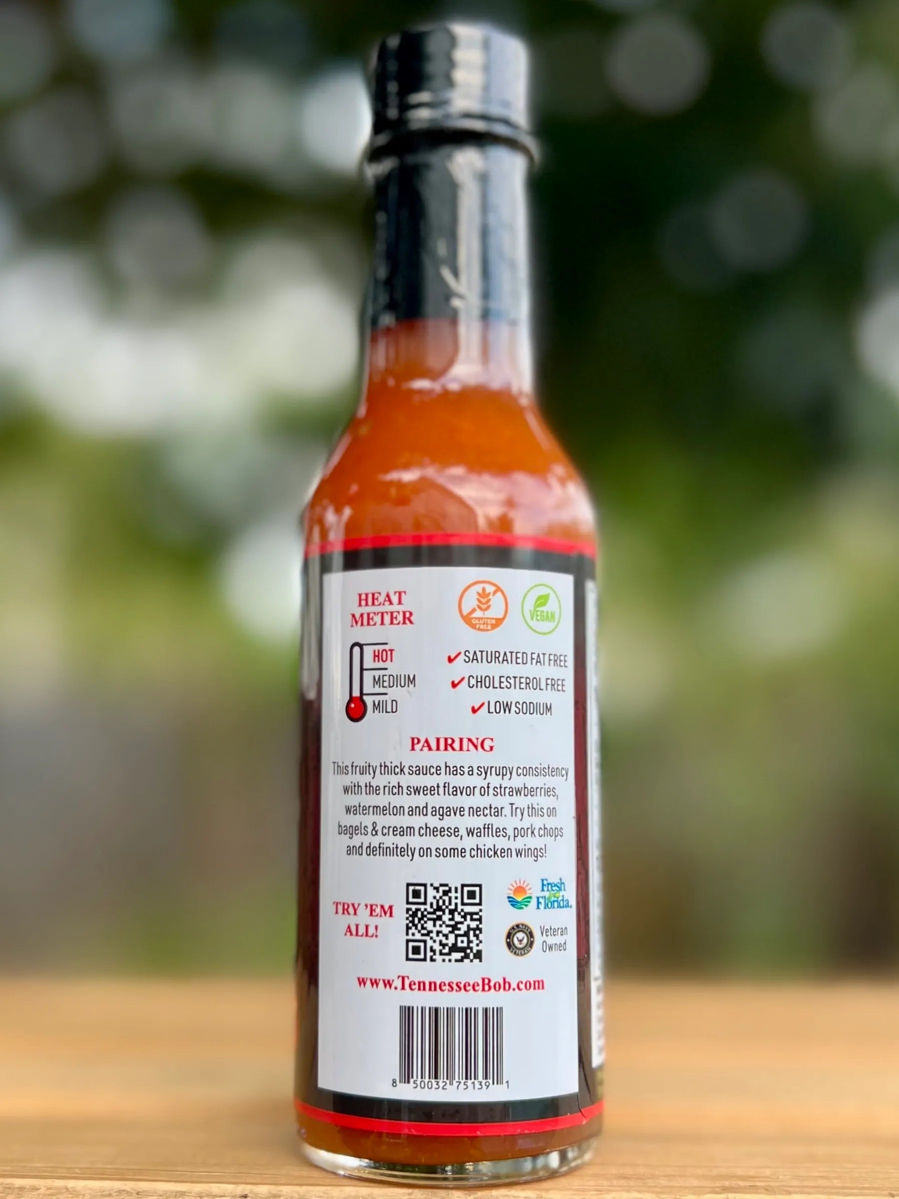 Hot sauce bottle with label on a wooden surface and blurred green background