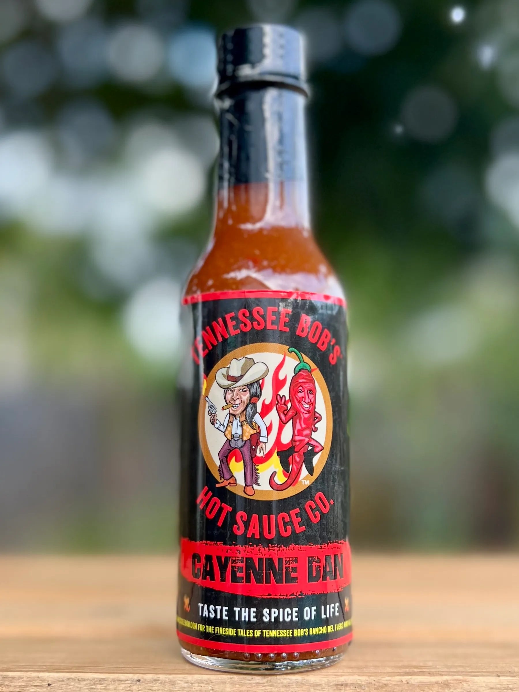 Bottle of Tennessee Bob's Cayenne Gan on a wooden surface with a blurred green background