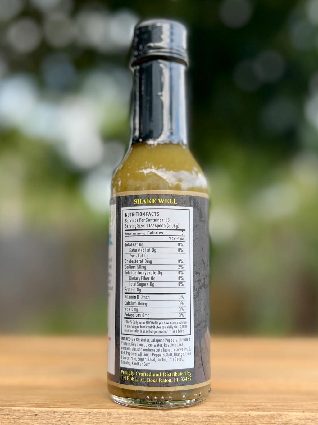 Bottle of chimichirri sauce with a label on a wooden surface and blurred green background