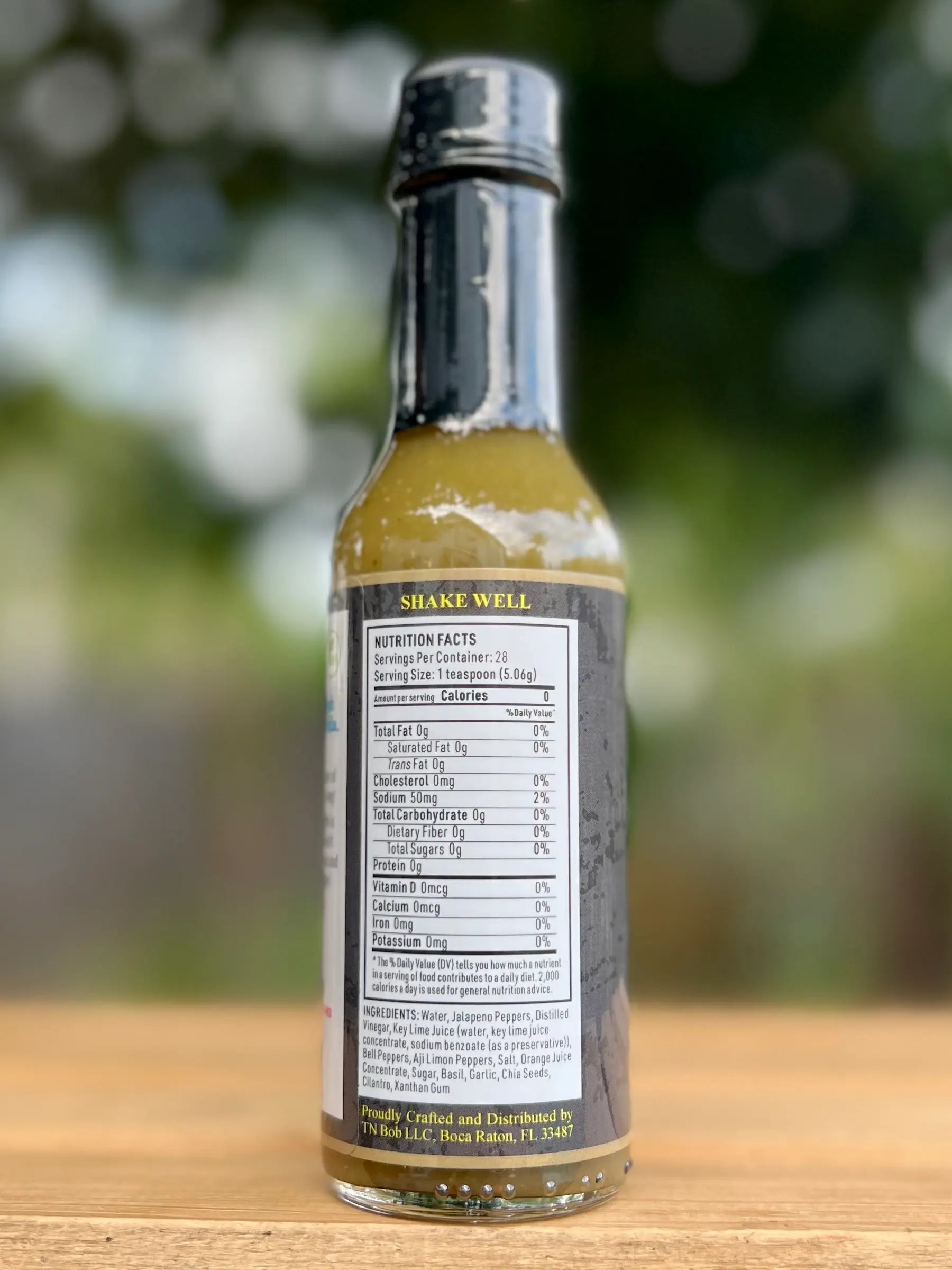Bottle of chimichirri sauce with a label on a wooden surface and blurred green background