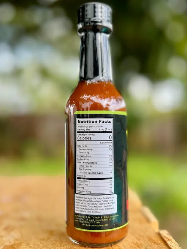 Hot sauce bottle with nutrition facts label, glass packaging, spicy condiment, zero calories, outdoor background.
