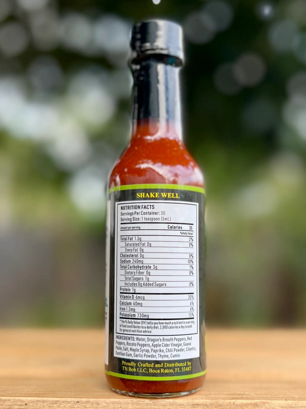 Hot sauce bottle with label on a wooden surface and blurred green background