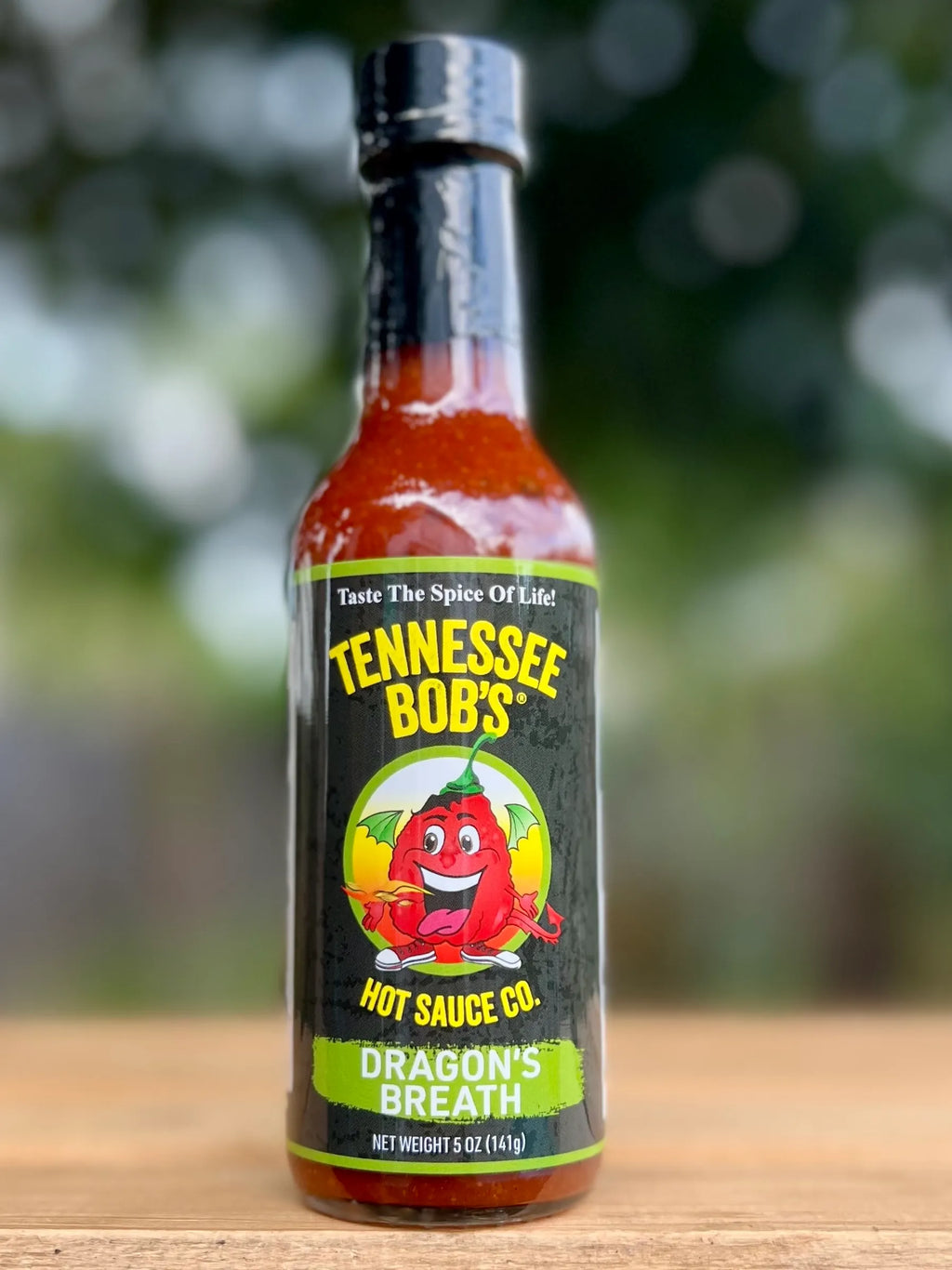 Bottle of Tennessee Bob's Dragon's Breath hot sauce on a wooden surface with a blurred natural background