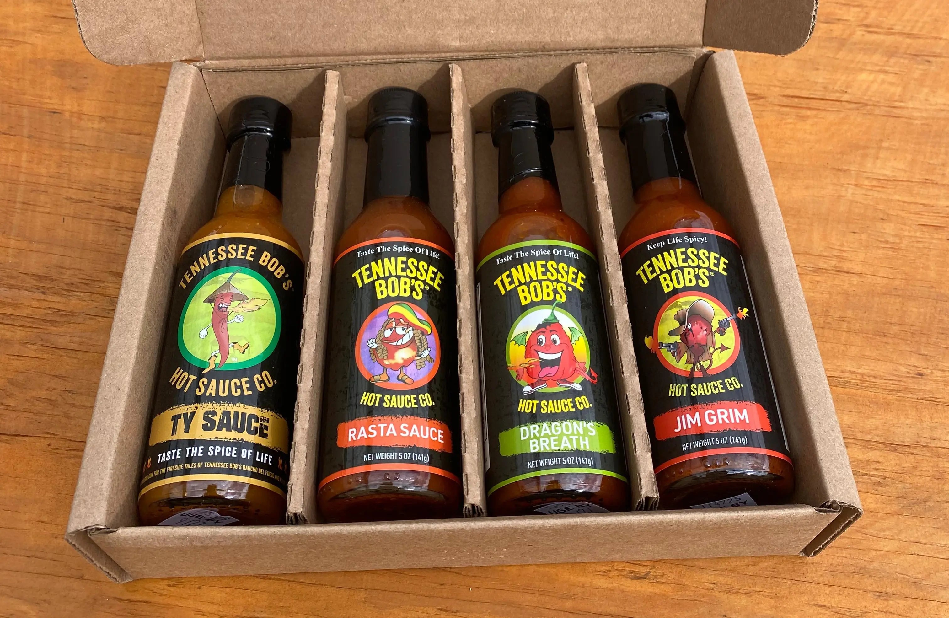 Four Tennessee Bob's hot sauce bottles in a cardboard box, featuring Ty Sauce, Rasta Sauce, Dragon's Breath, and Jim Grim flavors.