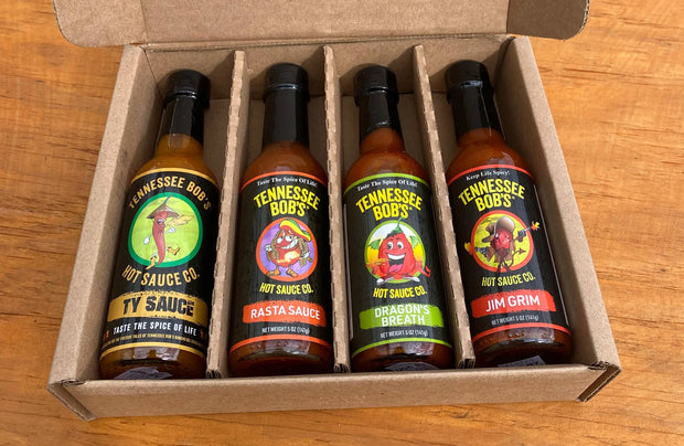 Four Tennessee Bob's hot sauce bottles in a cardboard box, featuring Ty Sauce, Rasta Sauce, Dragon's Breath, and Jim Grim flavors.