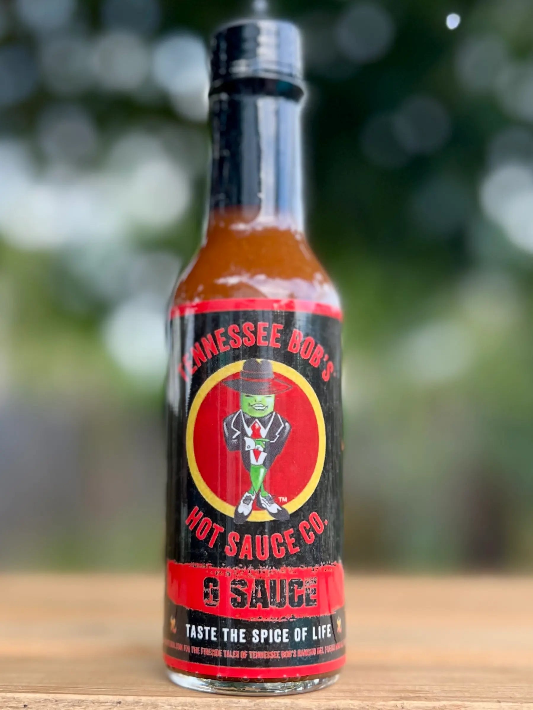 Bottle of Tennessee Bob's Hot Sauce Co. hot sauce on a wooden surface with a blurred natural background