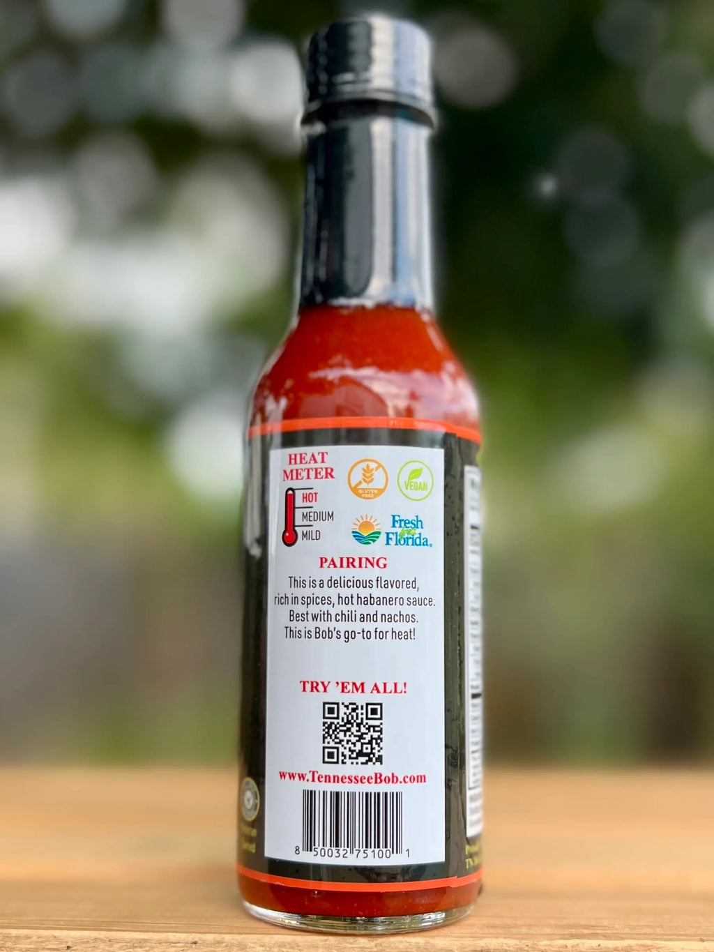 Hot sauce bottle with label on a wooden surface and blurred green background