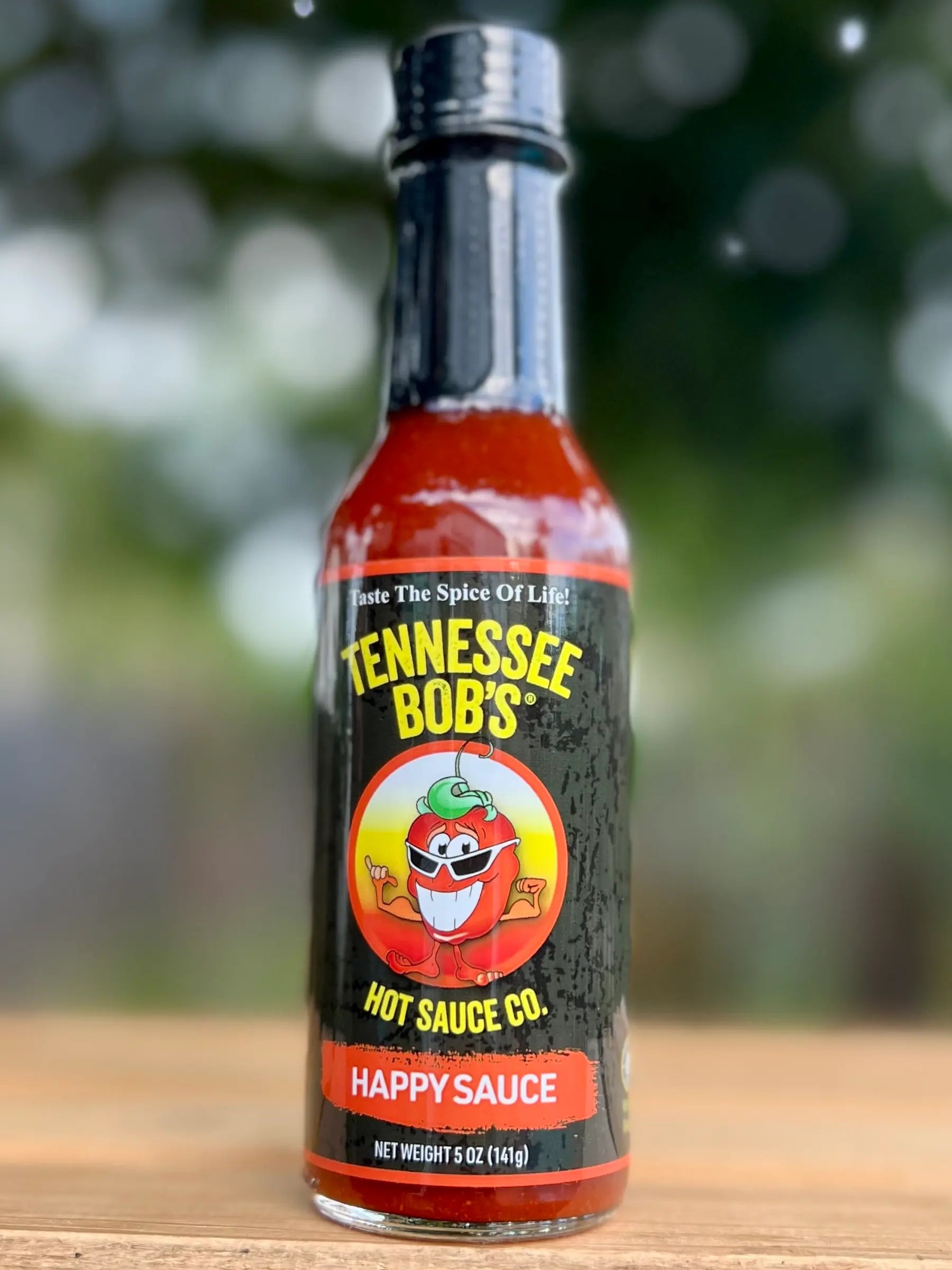 Bottle of Tennessee Bob's Hot Sauce Co. Happy Sauce on a wooden surface with a blurred natural background