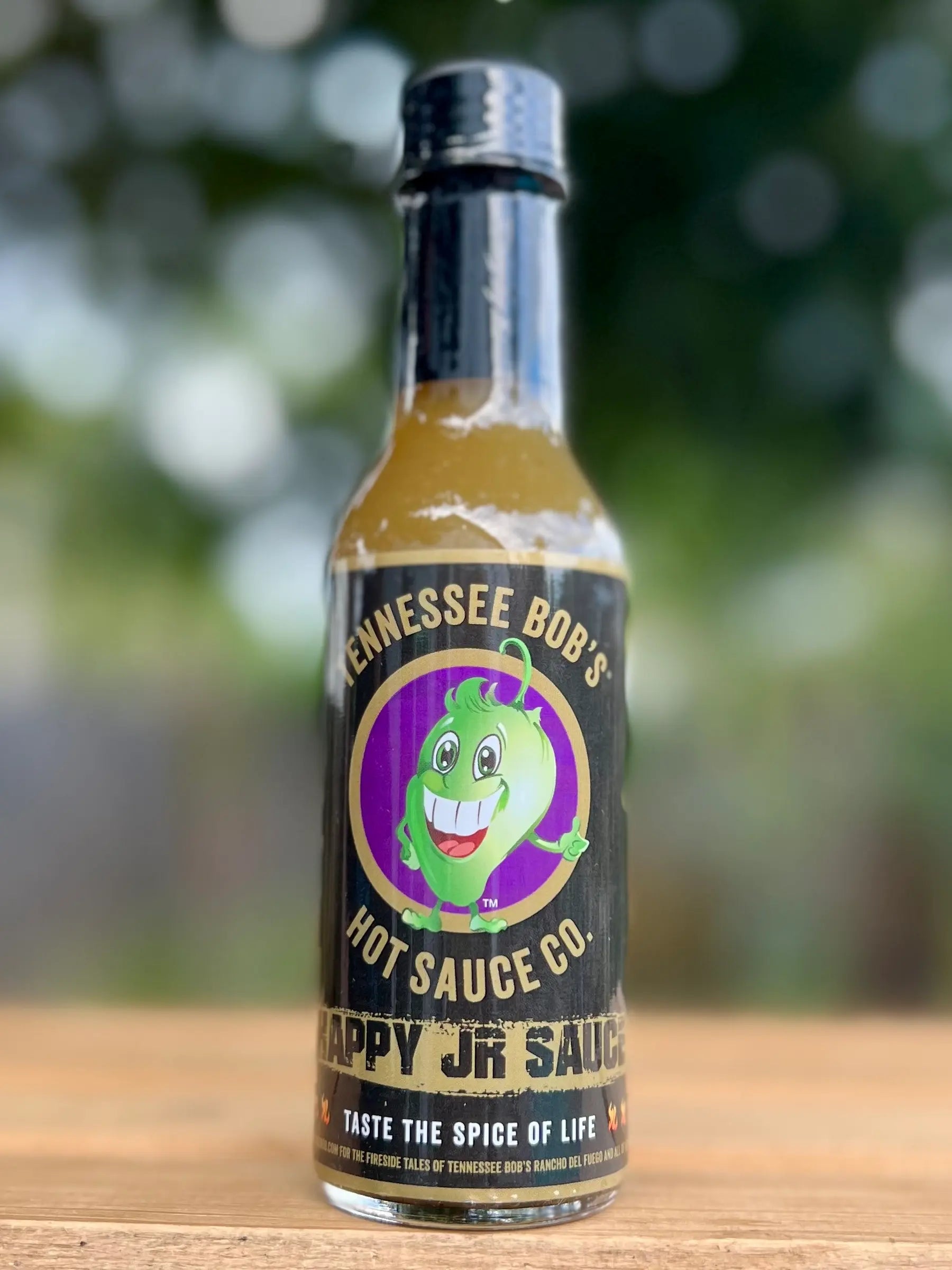 Bottle of Tennessee Bob's Hot Sauce Co. on a wooden surface with a blurred natural background