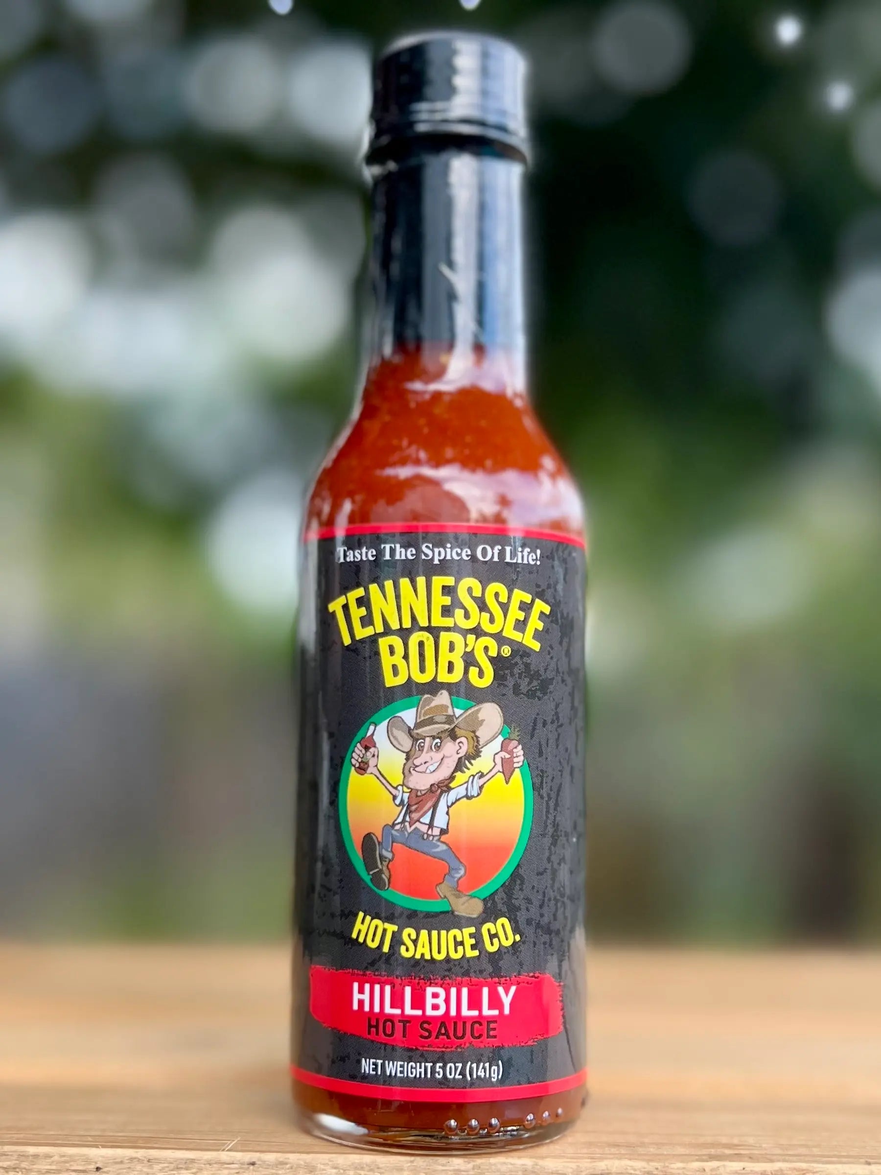 Bottle of Tennessee Bob's Hillbilly Hot Sauce on a wooden surface with a blurred natural background