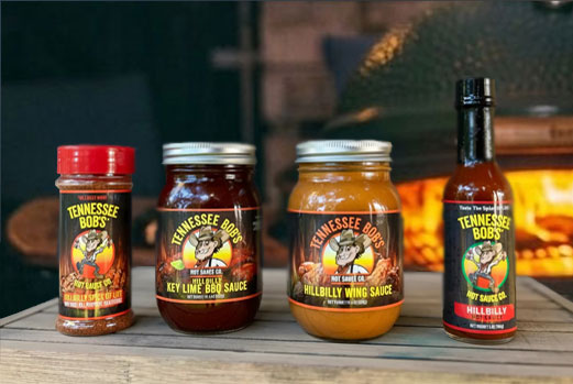 Tennessee Bob's barbecue sauces and spices set in front of a rustic outdoor grill.