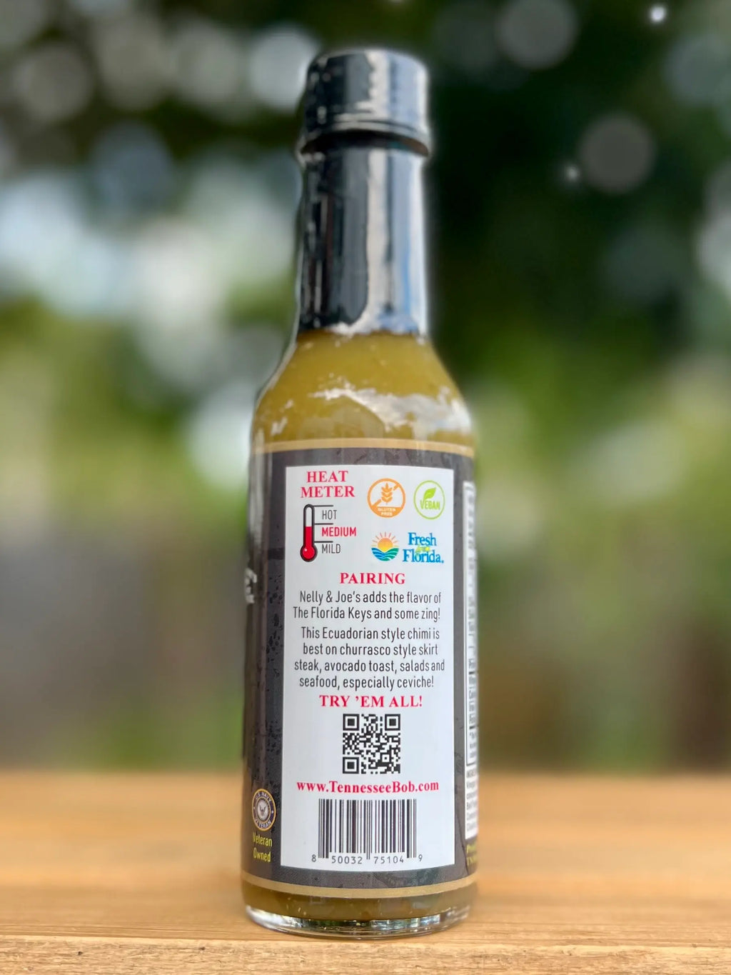 Bottle of hot sauce with label on a wooden surface and blurred green background