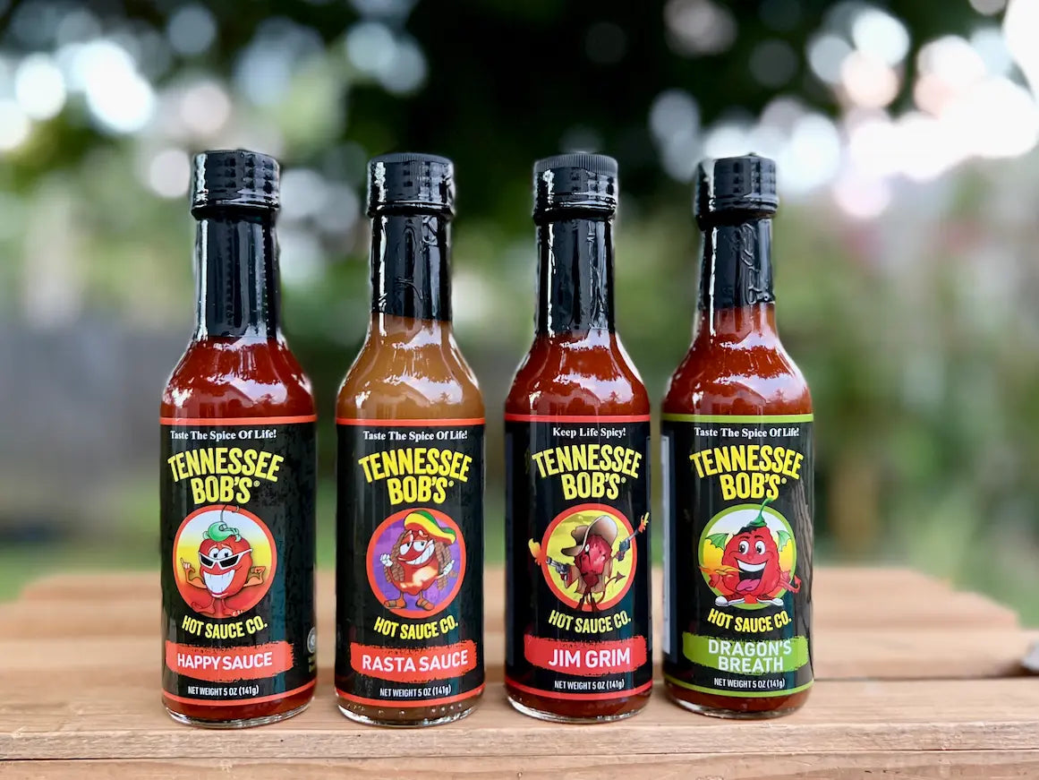 Four bottles of Tennessee Bob's hot sauce on a wooden surface with a blurred natural background