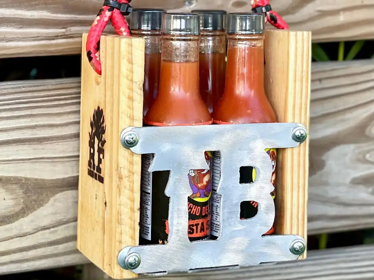 Wooden bottle opener with three bottles of hot sauce and a can of beer on a wooden surface.