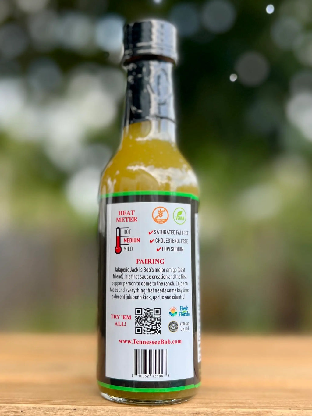 Bottle of hot sauce with a label on a wooden surface and blurred green background