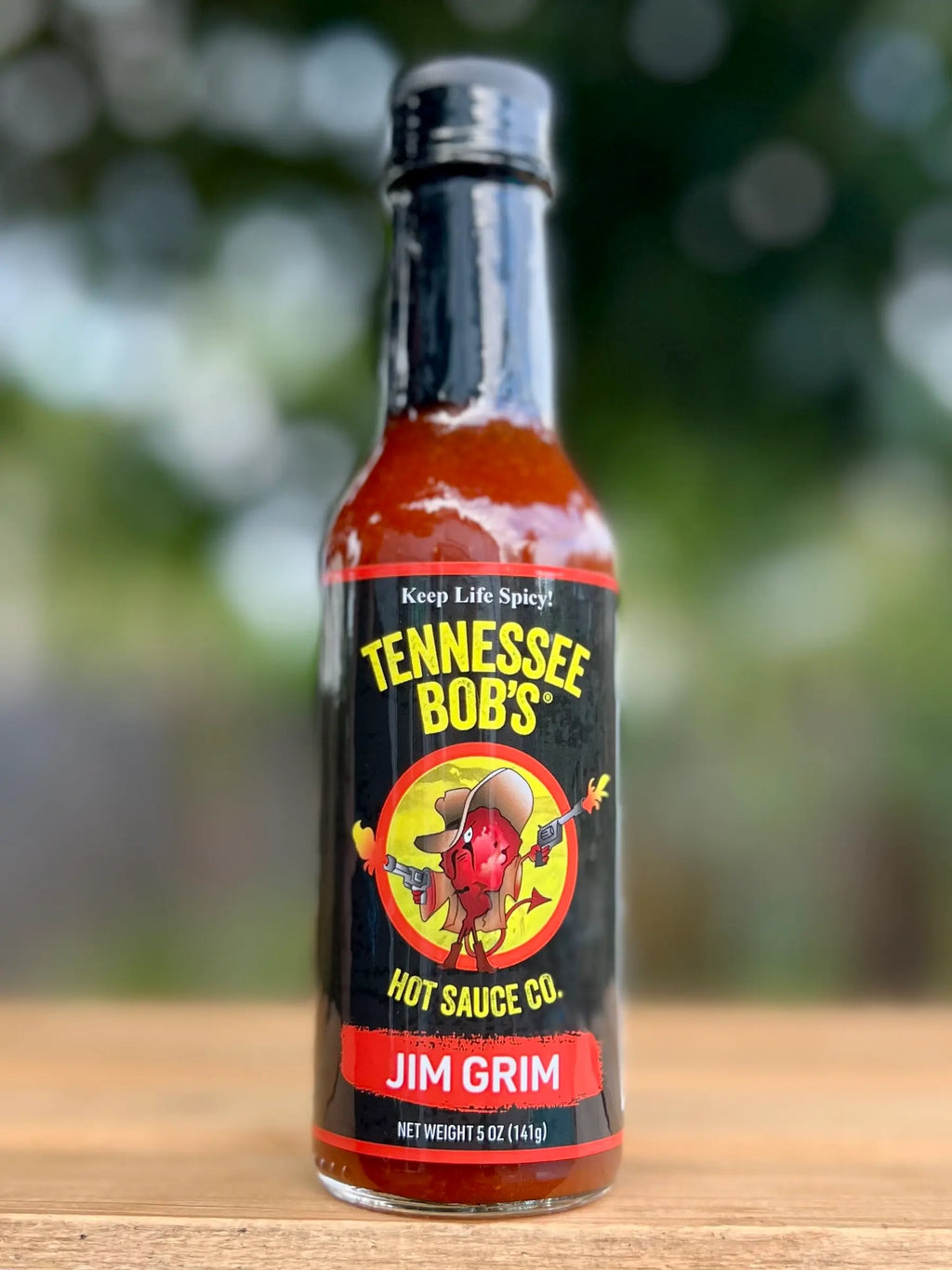 Bottle of Tennessee Bob's Hot Sauce Co. Jim Grim on a wooden surface with a blurred natural background