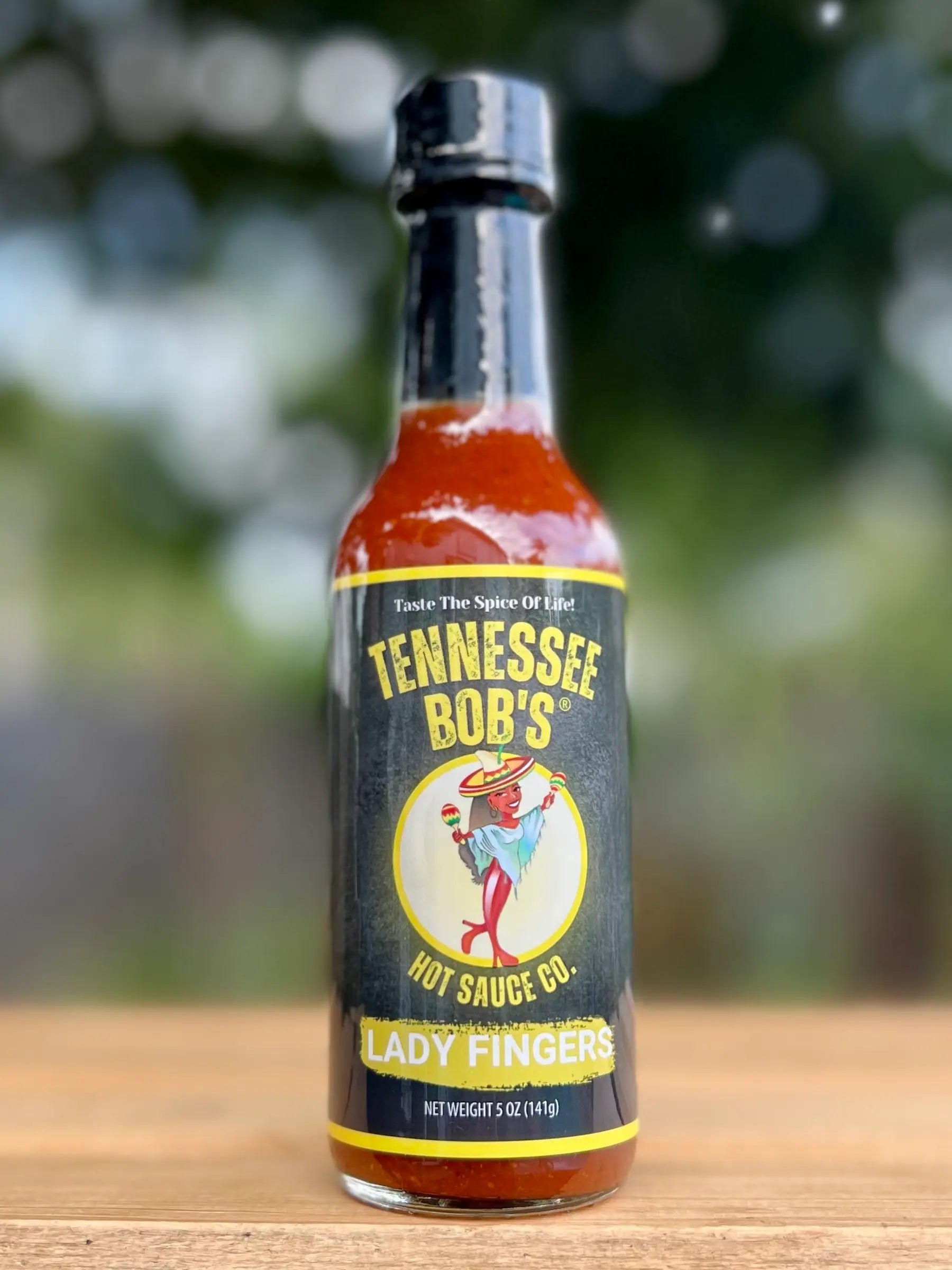 Bottle of Tennessee Bob's Lady Fingers hot sauce on a wooden surface with a blurred green background
