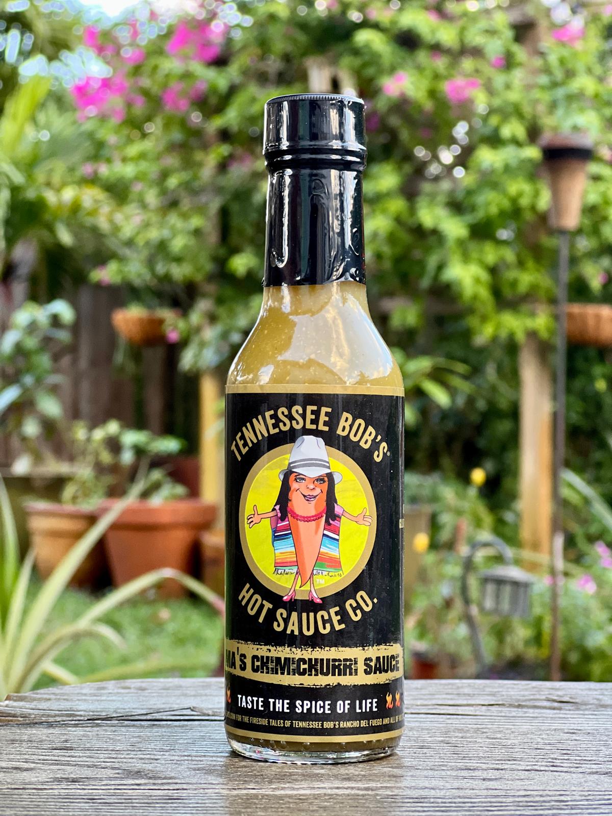 Tennessee Bob's chimichurri sauce bottle on a wooden table with garden background.