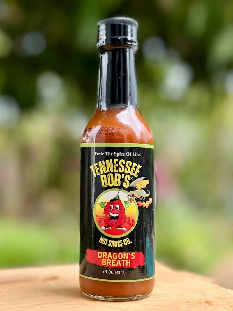 Tennessee Bob's Dragon's Breath hot sauce bottle on a wooden surface with a blurred green background.