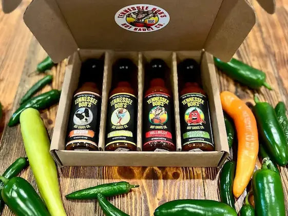 Tennessee Bob's hot sauce sampler pack with assorted fresh peppers on a wooden surface.