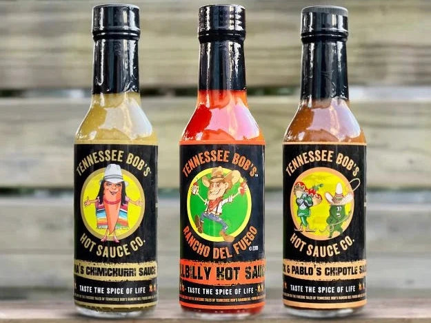 Three bottles of Tennessee Bob's Hot Sauce Co. hot sauce with colorful labels on a blurred background.