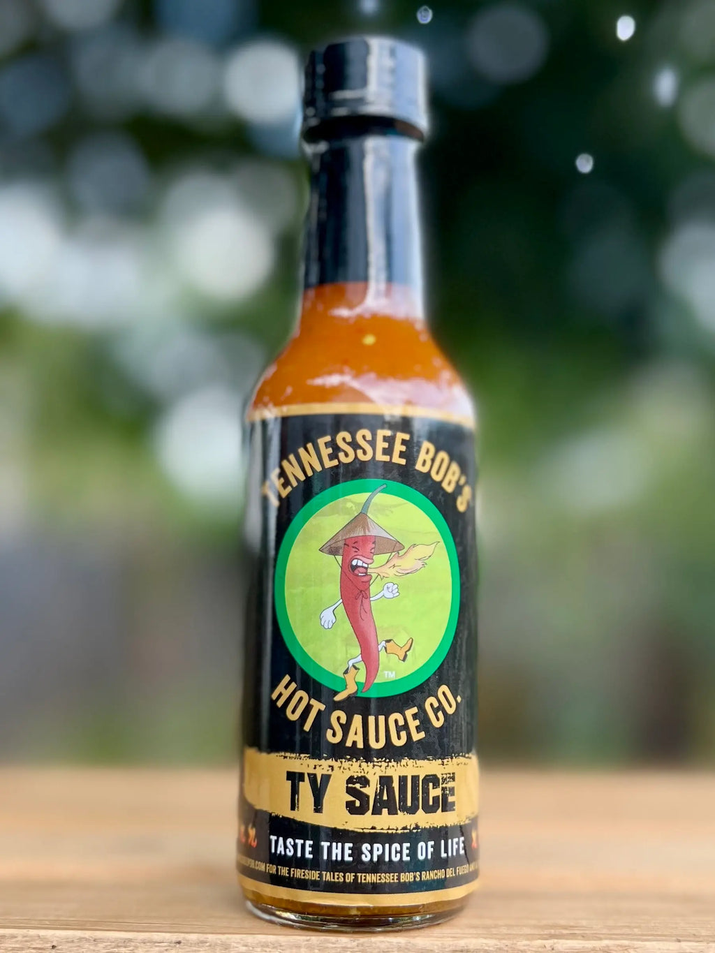 Bottle of Tennessee Bob Hot Sauce Co. Ty Sauce on a wooden surface with a blurred green background