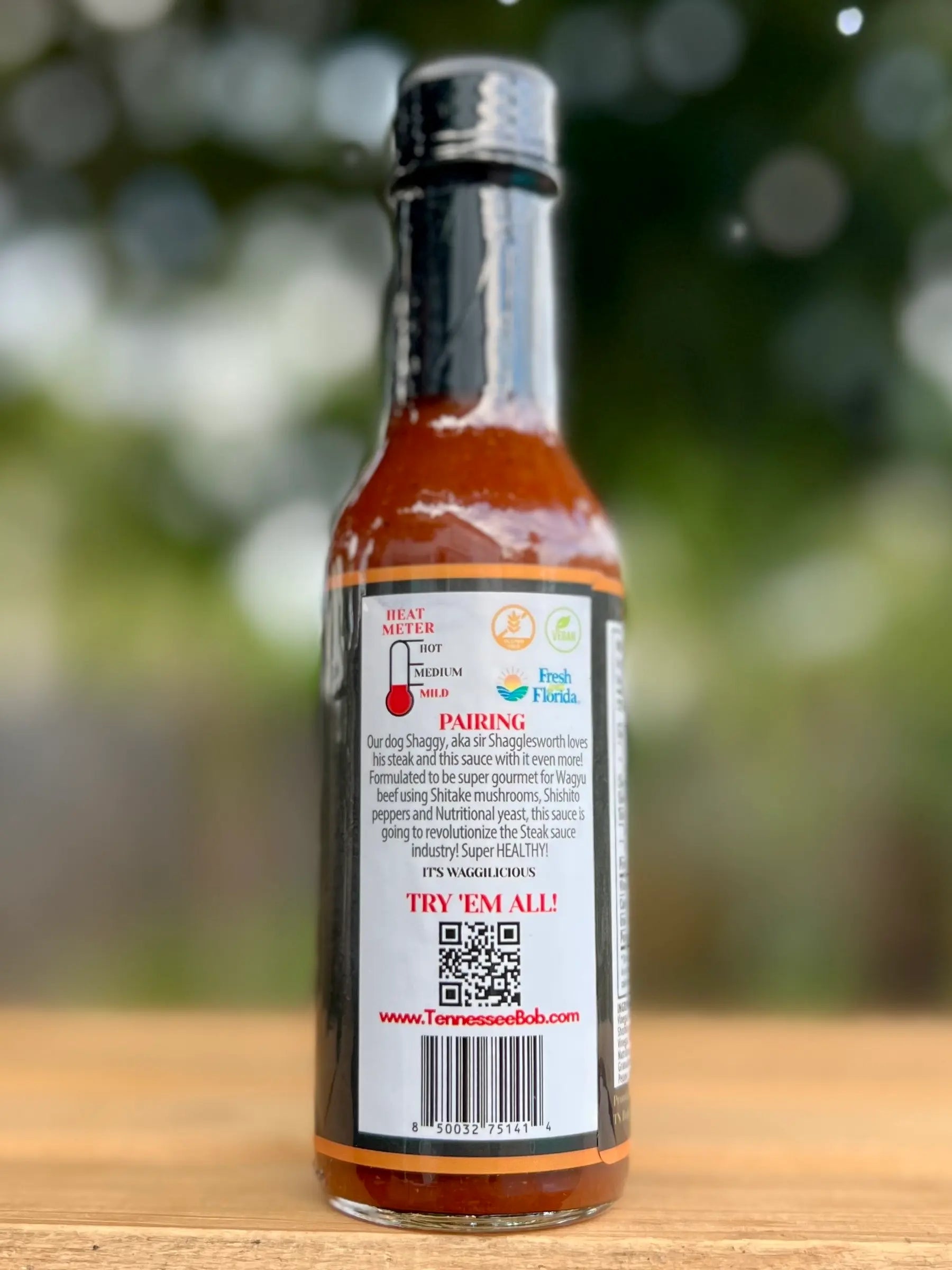 Hot sauce bottle with label on a wooden surface and blurred green background