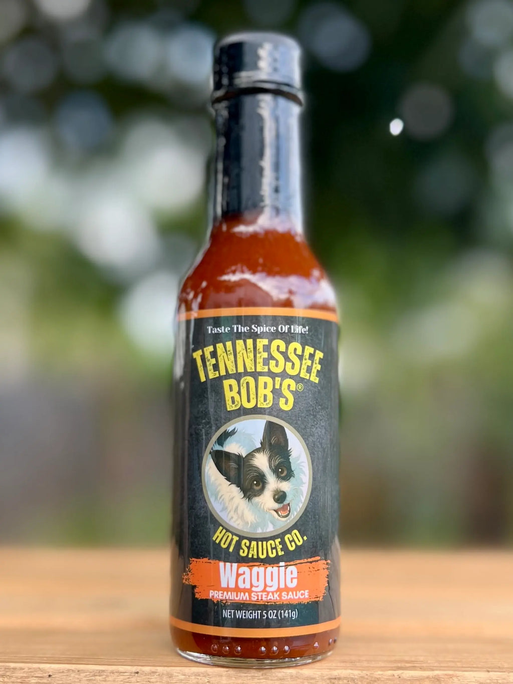Bottle of Tennessee Bob's hot sauce on a wooden surface with a blurred natural background