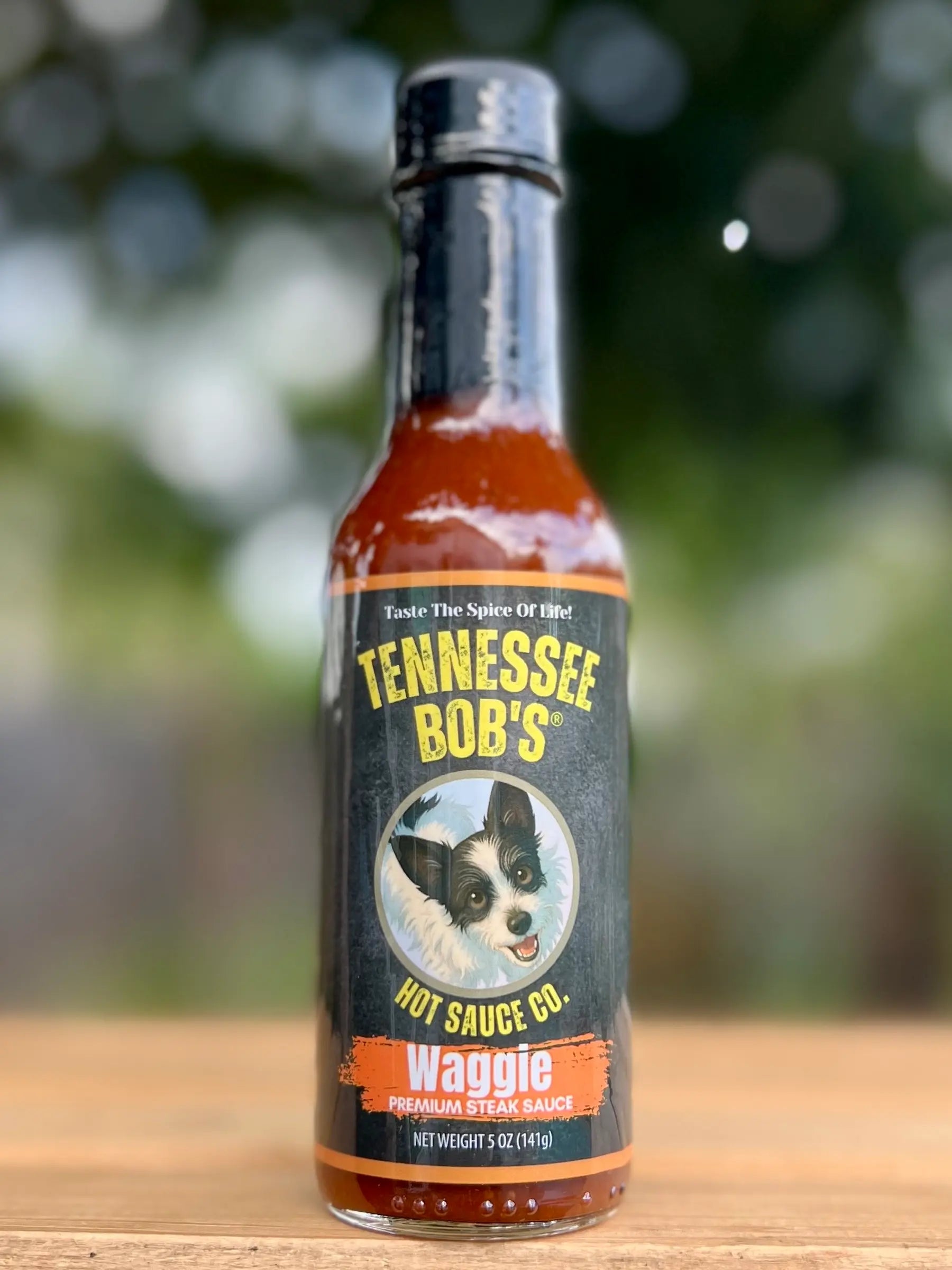 Bottle of Tennessee Bob's hot sauce on a wooden surface with a blurred natural background